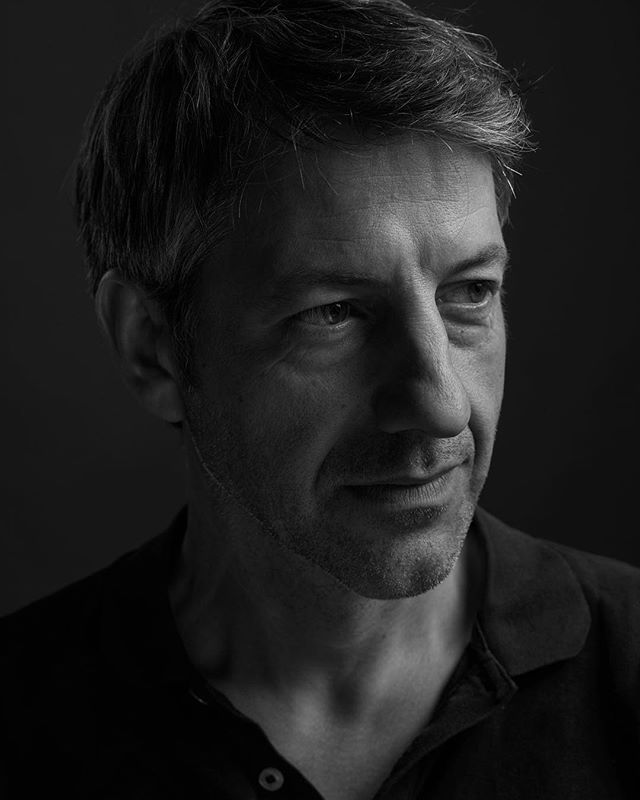 A close-up, monochrome portrait of a man against a dark background, conveying a sense of seriousness and contemplation.
