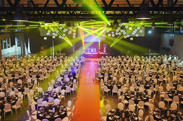 A large ballroom set for a banquet with round tables, chairs, and a stage illuminated by stage lights.