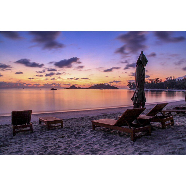 A serene beach at sunset with deck chairs and calm ocean water for a relaxing tropical getaway.
