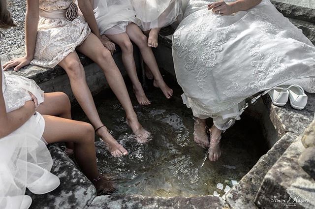 Bride and bridesmaids celebrate a wedding by dipping their feet into a water feature, creating a candid and joyous scene.