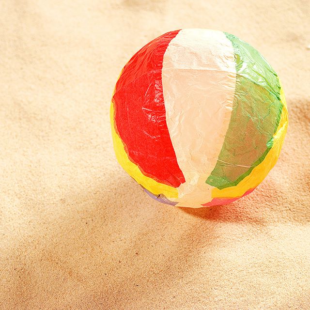 A colorful beach ball sits on a sandy beach, evoking summer fun and childhood games.