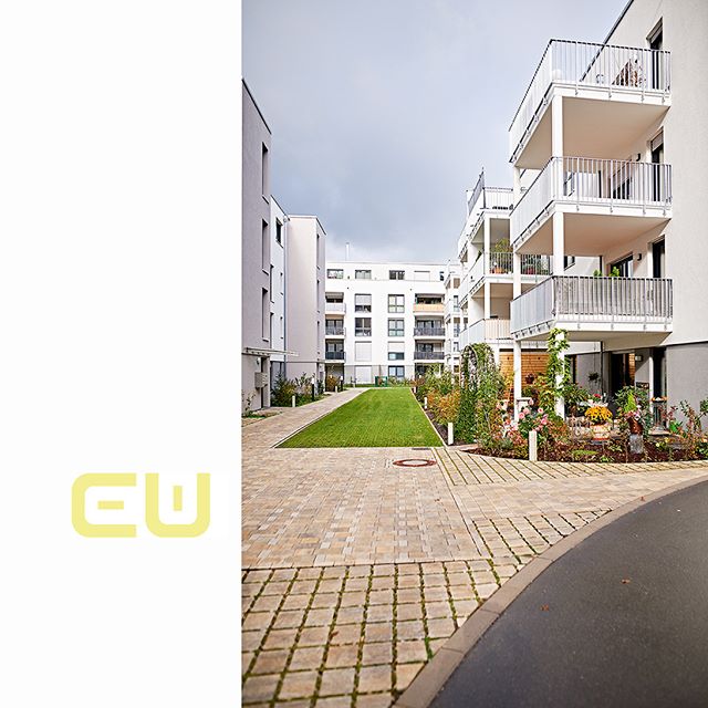 A modern residential building complex with a central green courtyard and balconies on a cloudy day, showcasing urban design.