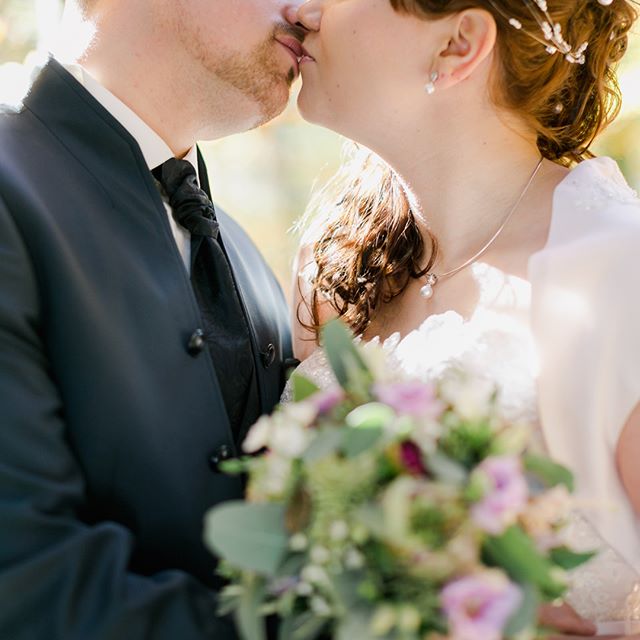 A bride and groom share a tender kiss during their wedding, with a beautiful bouquet in the foreground.