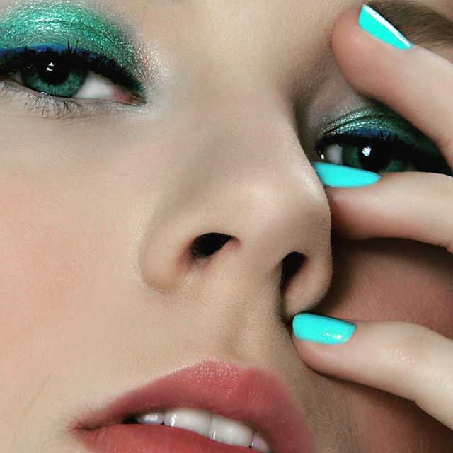 A vibrant closeup showcases teal makeup and matching nails, offering a fresh take on beauty aesthetics.
