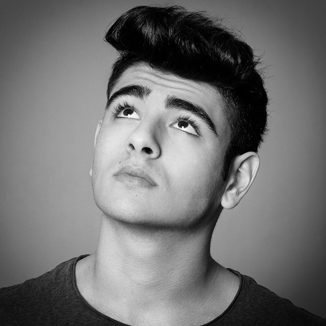 Black and white studio portrait of a young man looking up, with a contemplative expression.