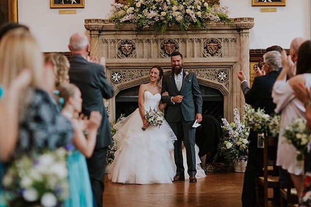 A bride and groom walk down the aisle after their wedding, surrounded by applauding guests.