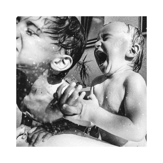 A playful black and white photo captures two children in the bath, enjoying a moment of sibling fun and splashing.