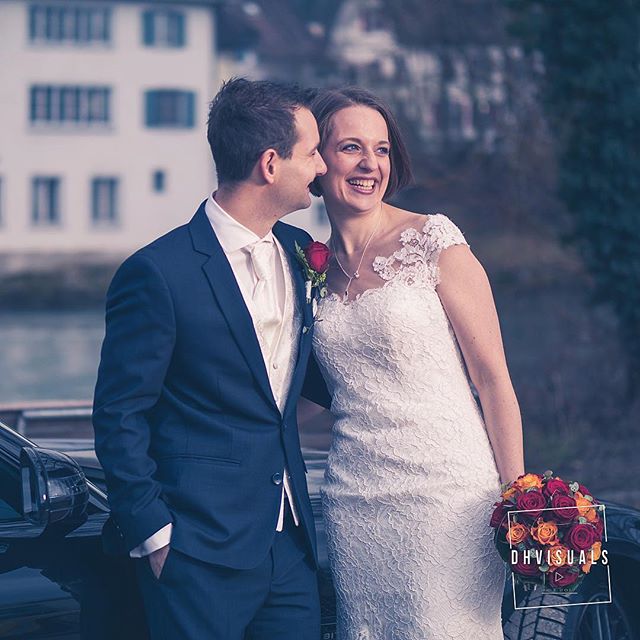 A happy couple celebrates their wedding day outdoors, sharing a loving moment next to a car with flowers.