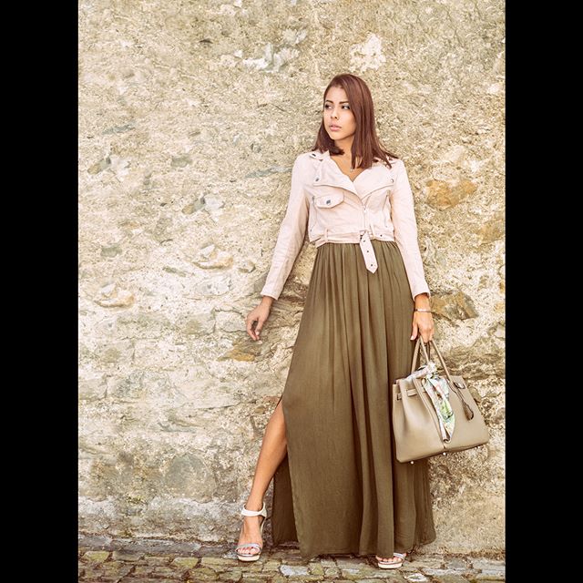 A stylish woman poses in a maxi dress and leather jacket for a fashion editorial.