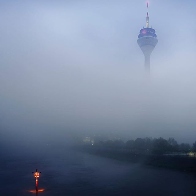 The Dusseldorf TV Tower rises through heavy fog on the Rhine River, Germany, creating a mysterious cityscape.