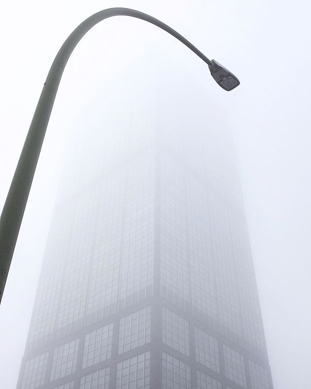 A tall building disappears into the fog, standing behind a street light.
