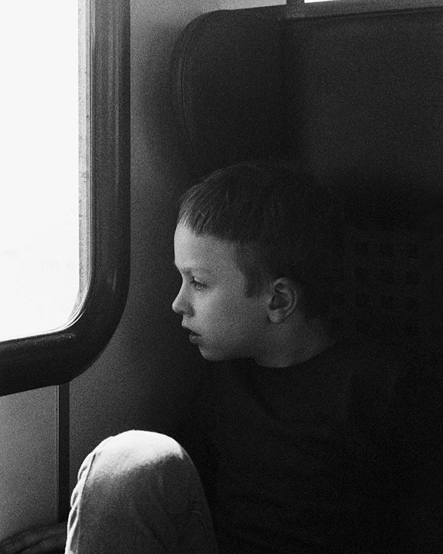 A young boy gazes out a train window, lost in thought, in a black and white evocative scene.