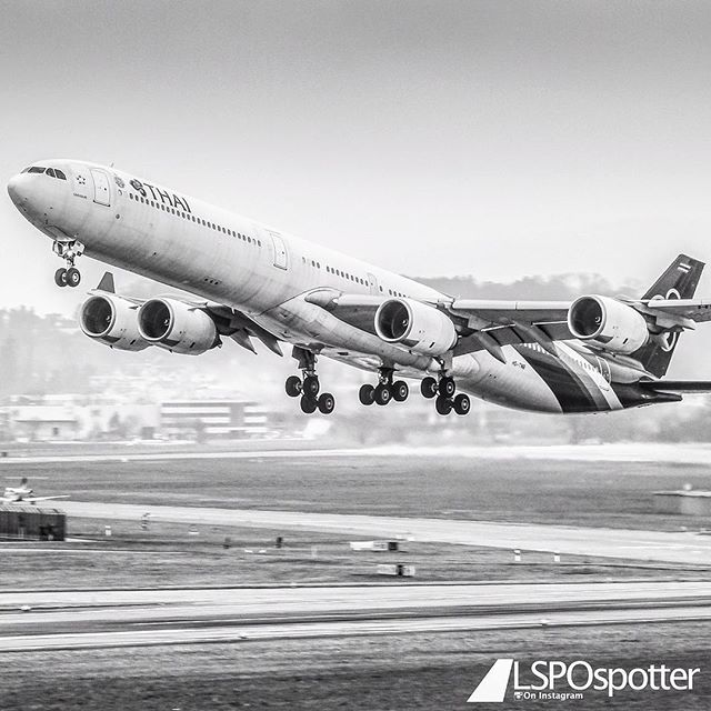 A Thai Airways airplane takes off from a runway in a black and white photograph.