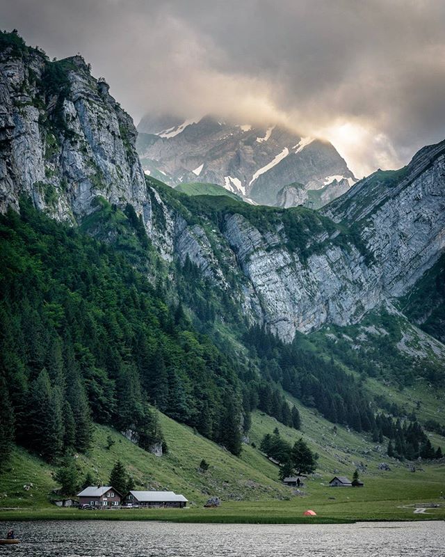 Scenic mountain valley with a lake, traditional houses, and cloudy sky provides a tranquil nature scene.
