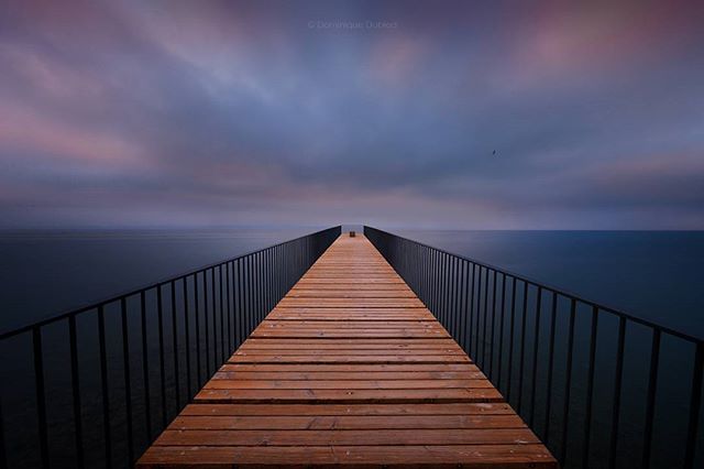 A long wooden pier extends into the calm sea under a moody sky, evoking peace and tranquility.