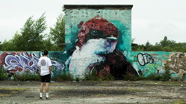 A man stands before a brick wall with a large bird graffiti mural in an urban setting.