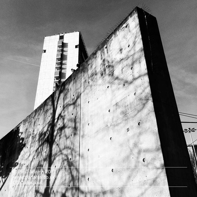 A striking black and white perspective of a tall concrete wall, with a building towering in the background.