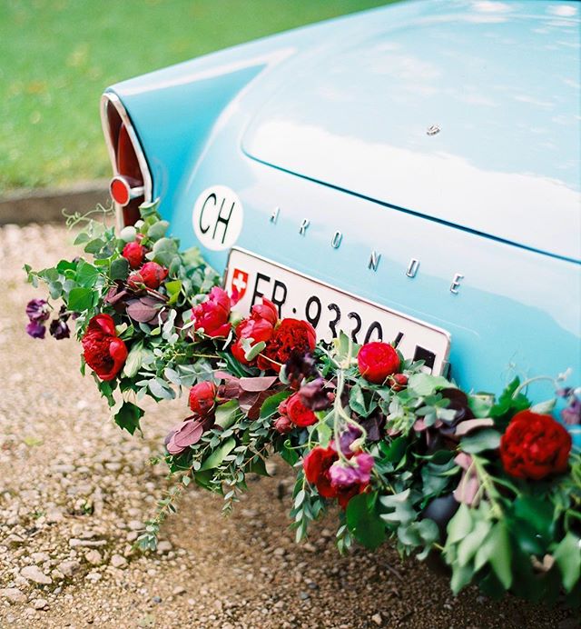 A light blue vintage car decorated with red and green flowers, perfect for a romantic wedding or getaway.
