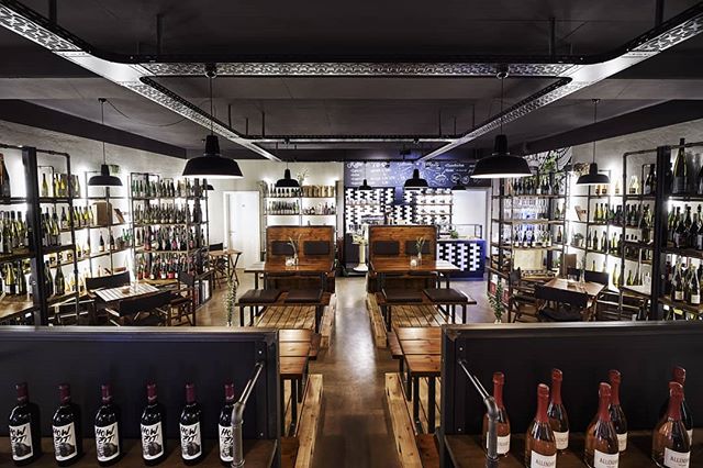 Interior view of a modern wine shop featuring shelves of wine bottles, wooden tables, and seating for a relaxed tasting experience.