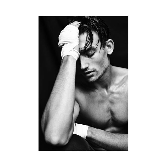 A shirtless boxer with hand wraps sits with his head in his hand in a black and white studio shot.