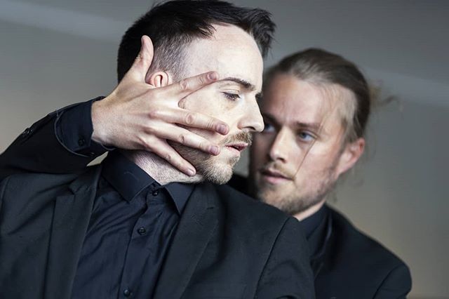 Two male models pose in a modern studio setting, conveying intense emotions for a fashion campaign.