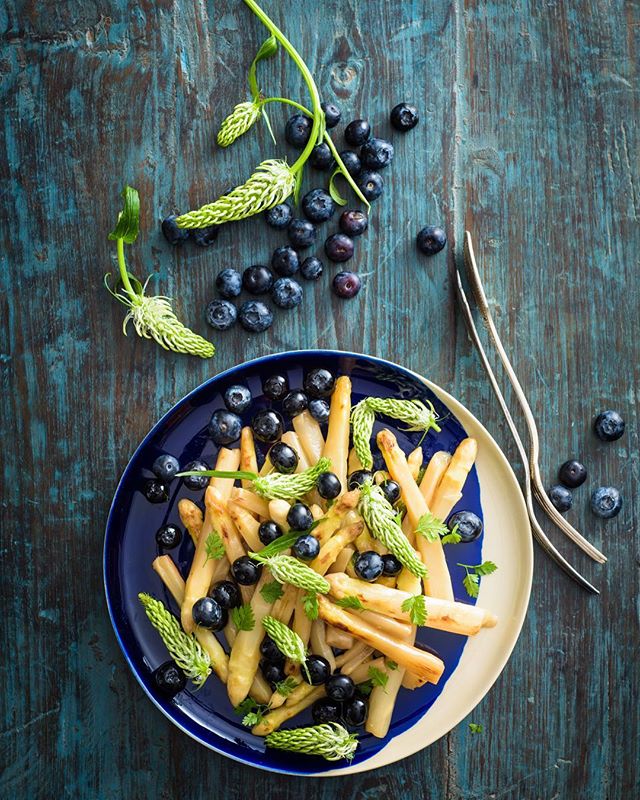 A vibrant plate of asparagus and blueberries on a rustic blue wooden table.
