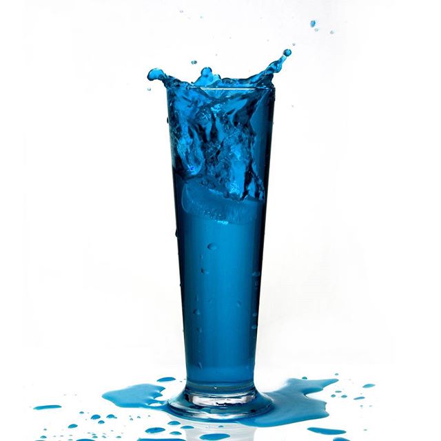 A glass splashes blue liquid on a white backdrop for a dynamic and refreshing image.