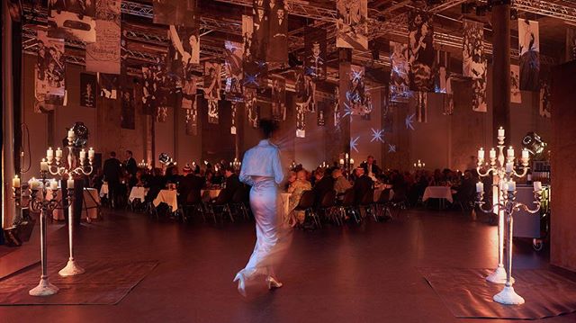 Elegant banquet hall scene with candelabras, people at tables, and a woman walking, creating a warm, intimate atmosphere.