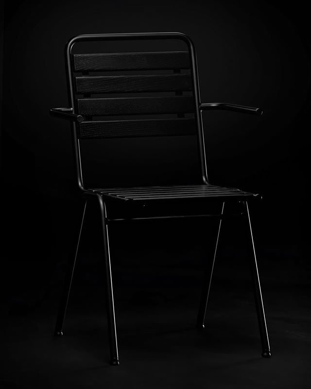 A modern black chair with a minimalist design stands elegantly against a dark background.