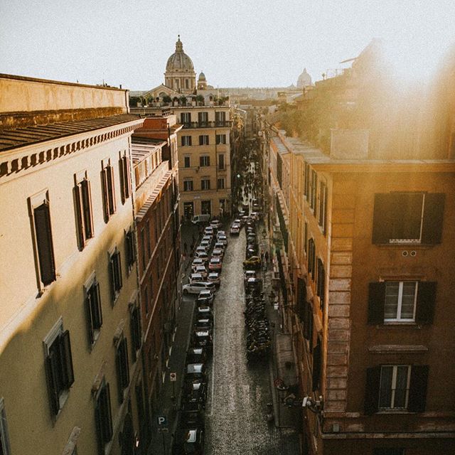 Aerial view of a charming Rome street lined with historic buildings, leading to a dome in the distance.