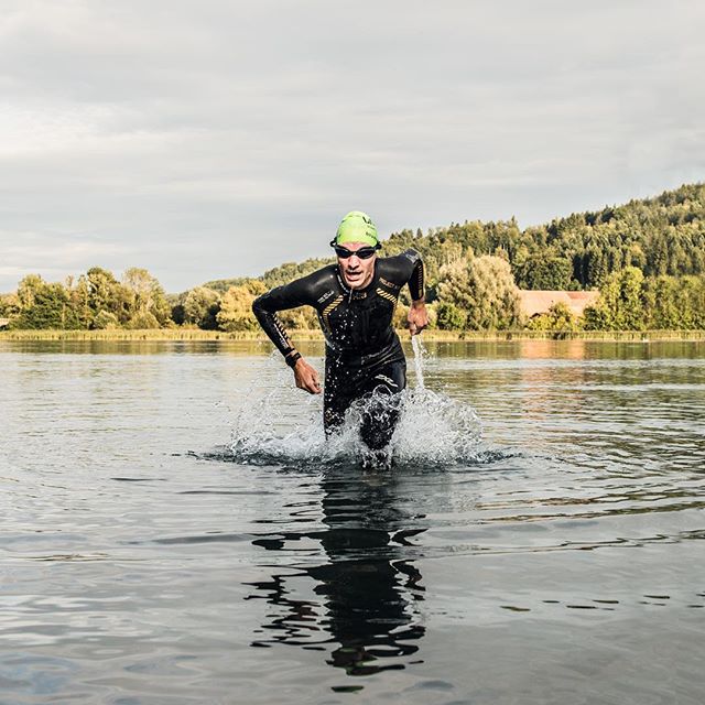 A determined triathlete runs out of the lake during a triathlon competition, showcasing endurance and fitness.