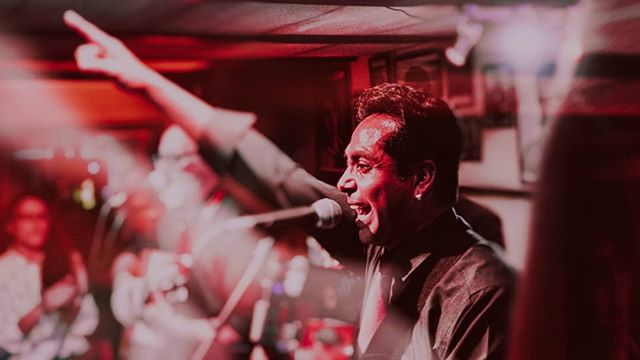 A singer passionately performs on stage, illuminated by vibrant red lights at a live concert.