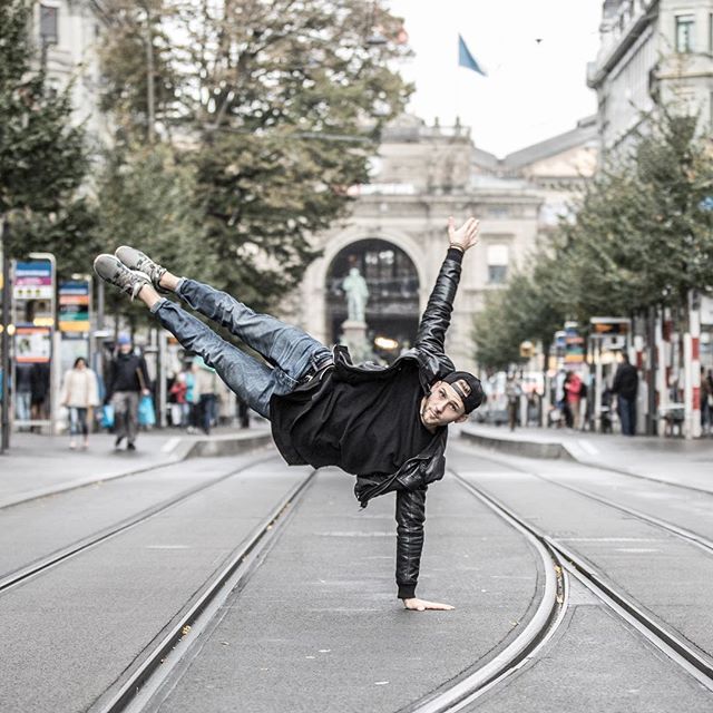 A street performer balances on one hand in an urban setting, showcasing his breakdancing skills and energetic lifestyle.
