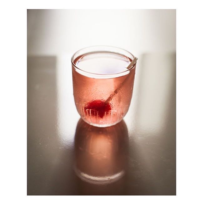 A glass of cocktail with a cherry sits on a reflective surface, perfect for a relaxing moment.