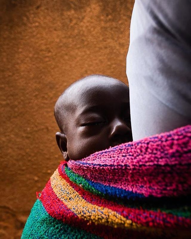A baby sleeps peacefully wrapped in a colorful cloth, close to their mother or caretaker.
