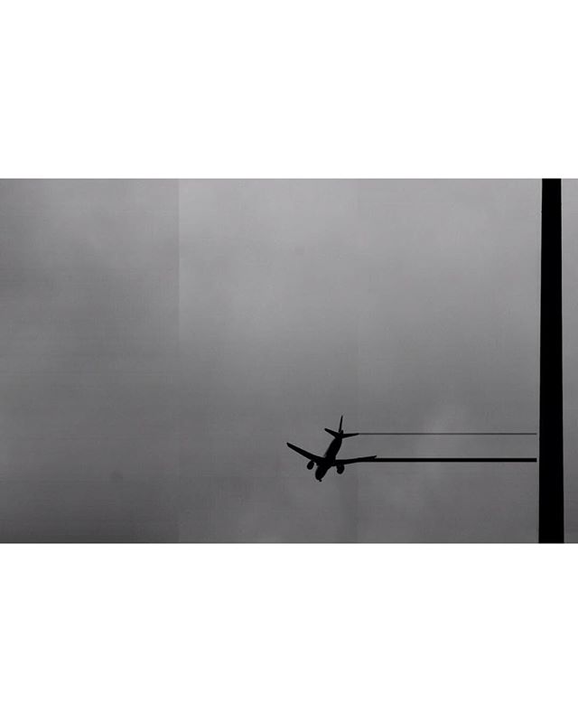 An airplane flies through a cloudy sky in silhouette against a grey backdrop.