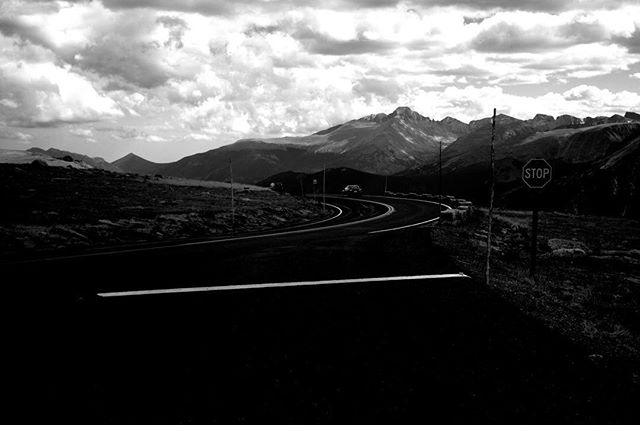 A winding road leads through a mountain landscape beneath a cloudy sky, with a stop sign marking the way.