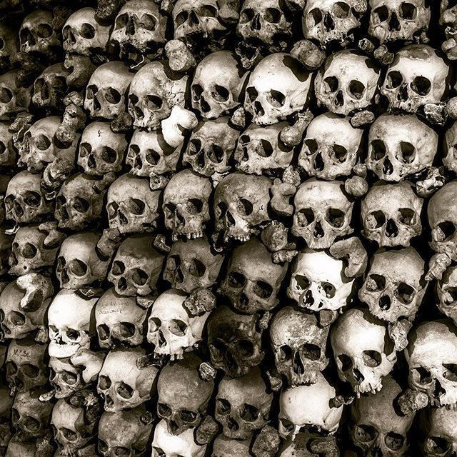 A sepia-toned close-up of a wall stacked with human skulls, creating a macabre and mysterious gothic background.