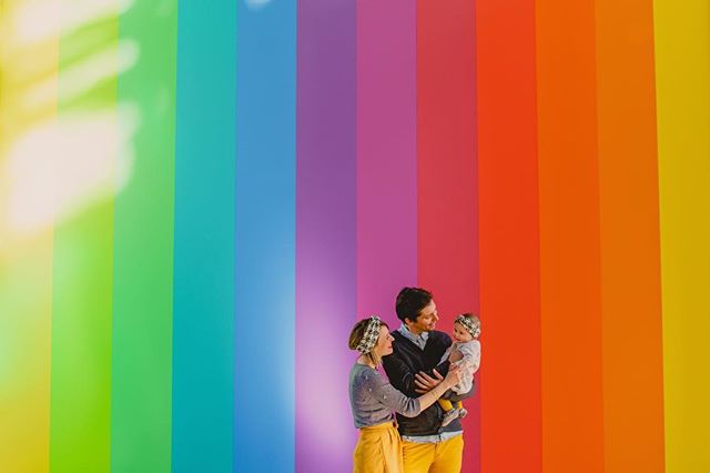 A happy family stands in front of a vibrant rainbow wall, showcasing unity and joy.
