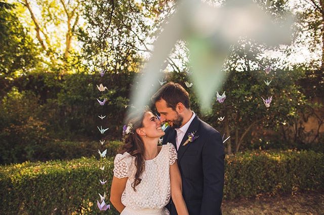 A bride and groom share a tender moment outdoors on their wedding day, surrounded by paper crane decorations.