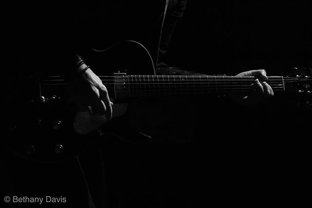 A musician plays an electric guitar in a dramatic, close-up black and white shot.
