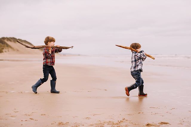 Two happy boys carrying sticks on the beach, enjoying outdoor play.