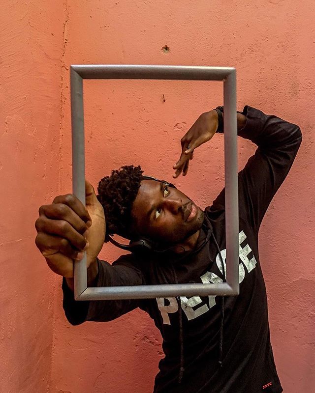 A young man confidently poses with a frame, adding depth and creativity to an urban backdrop.