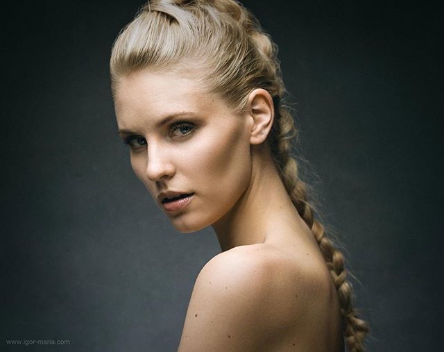 A blonde woman with a braid looks over her shoulder in a studio portrait.