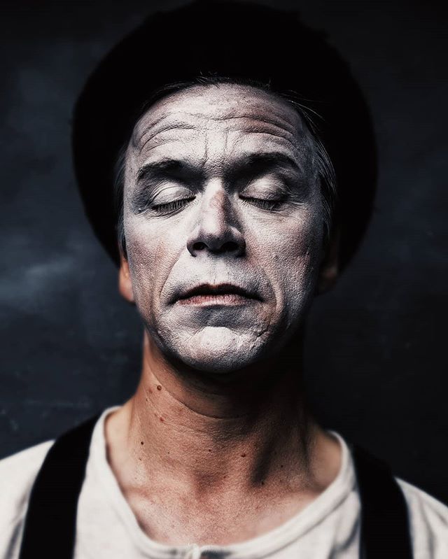 A mime artist with eyes closed in white face paint and a black hat evokes a sense of solemn emotion.