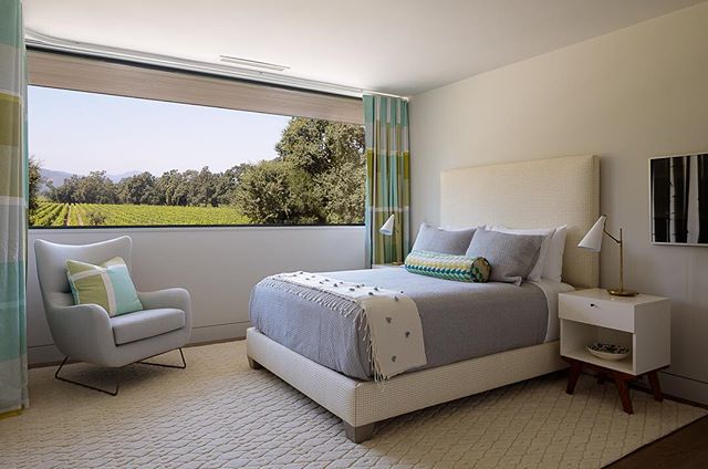 A bright bedroom showcases modern design with a comfortable bed, cozy armchair, and serene vineyard view.
