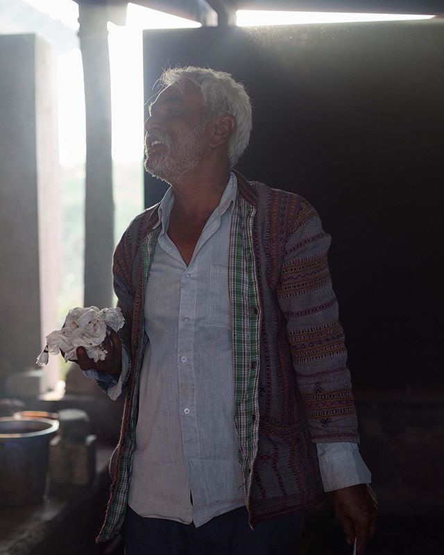 A senior man in shirt and patterned jacket holds cloth, bathed in natural light.