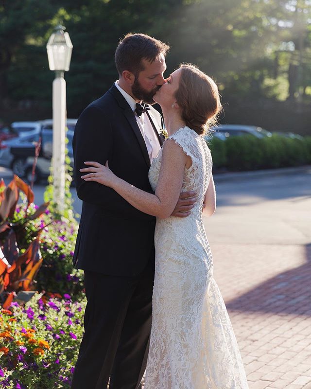 A bride and groom share a romantic kiss in a garden setting on their wedding day.
