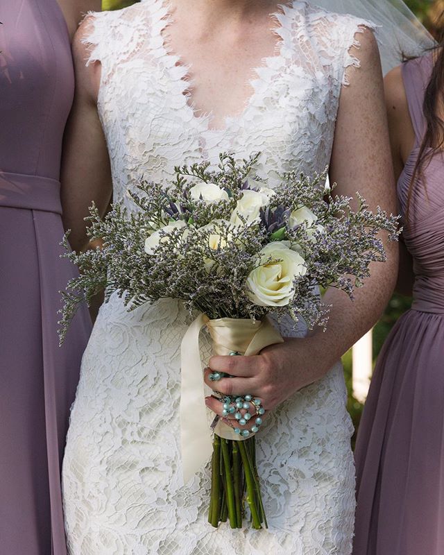 A bride in a lace gown holds a beautiful bouquet, surrounded by her bridesmaids on her wedding day.
