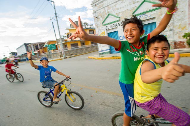 Four happy boys ride bikes and pose for the camera on a street in their neighborhood.